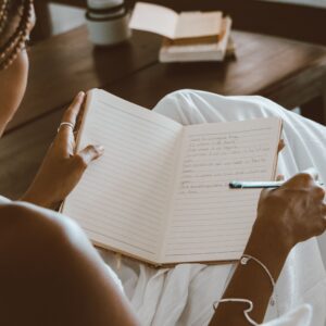 A black woman writes in a notebook, enjoying a calm indoor setting with natural light.