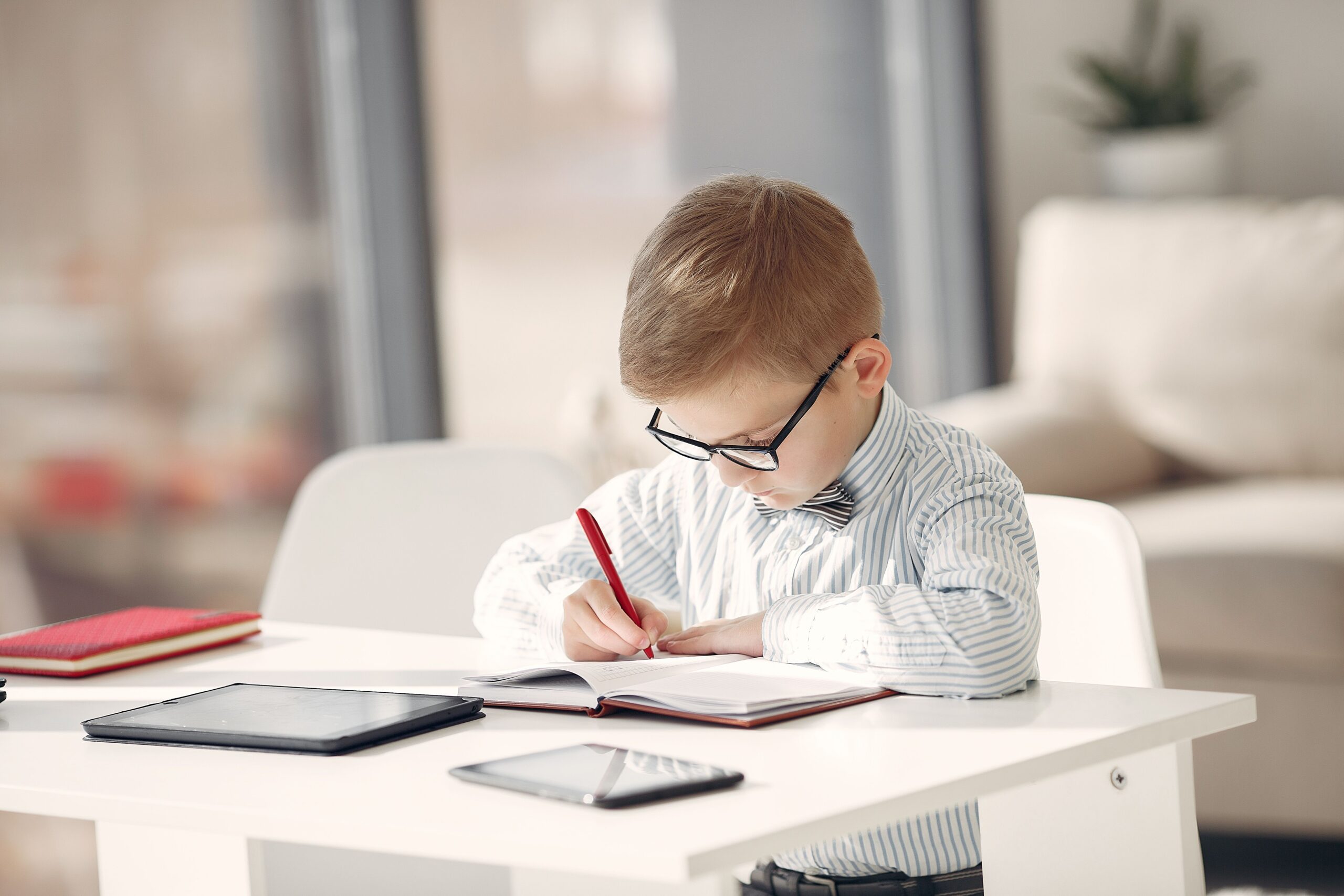 Focused employee boy taking notes in daily planner while working on project in front of gadgets in modern office