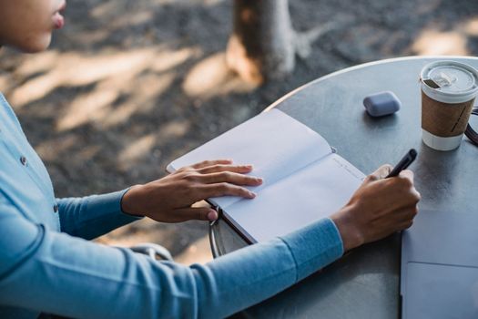 A close-up of a person writing notes in a notebook at an outdoor cafe table with a coffee cup.