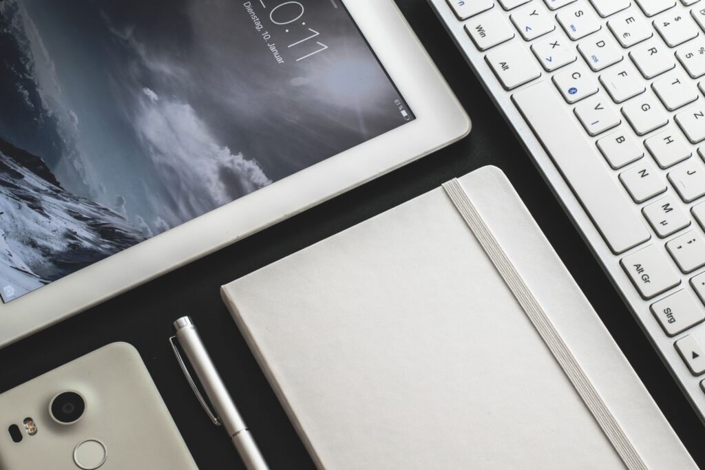 Overhead view of a modern desk setup featuring a tablet, smartphone, keyboard, and notebook.